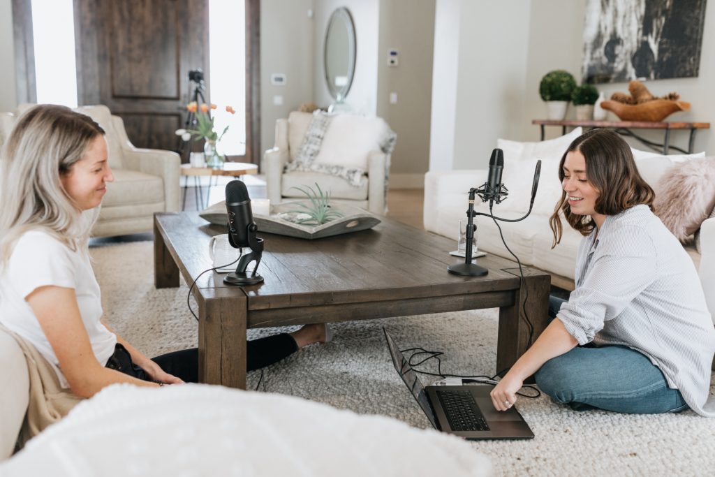 Le podcast crève l’écran 1 Deux femmes discutent autour d'une table basse sur laquelle sont disposés deux micros. L'une d'elle parle en regardant l'écran de son ordinateur portable.